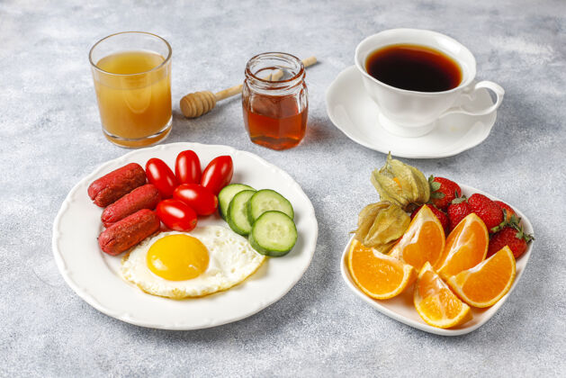 新鲜早餐盘子里有鸡尾酒香肠 煎蛋 樱桃番茄 糖果 水果和一杯桃子汁蛋黄食物蔬菜