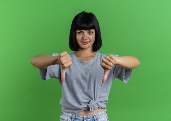 女孩年轻的黑发白人女孩拇指朝下 两只手被隔离在绿色背景上 留有复印空间复制二年轻