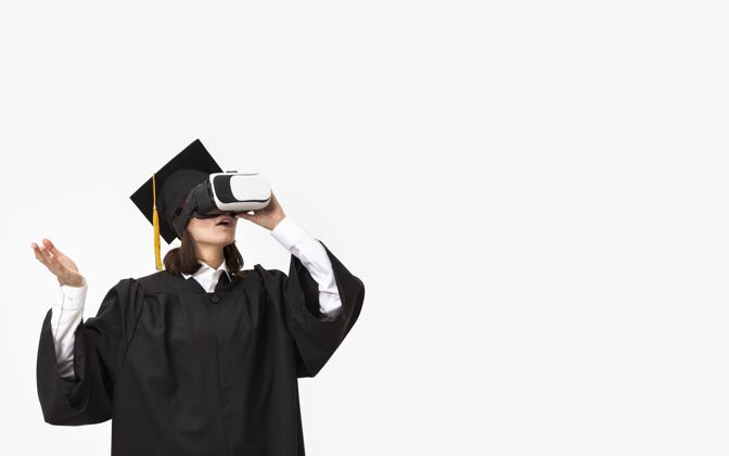 设备穿着毕业礼服戴毕业帽戴着虚拟现实耳机的女人仿真技术虚拟现实
