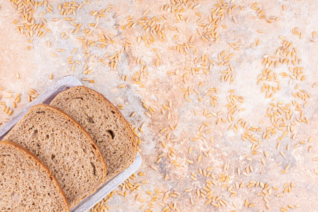 顶视图在大理石背景上 在木盘上的切片面包旁边撒上谷物小麦营养面包