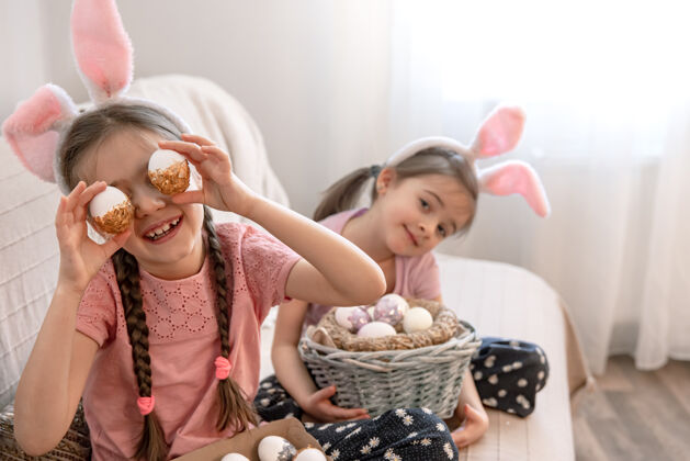 姿势有兔子耳朵的小姐妹们 家里的沙发上放着复活节彩蛋节日准备鸡蛋