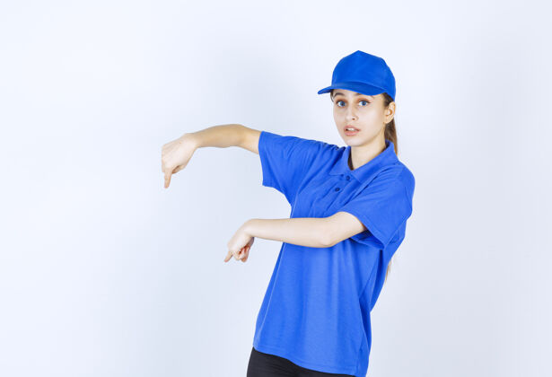 姿势穿蓝色制服的女孩在展示下面的东西地面工人工作人员