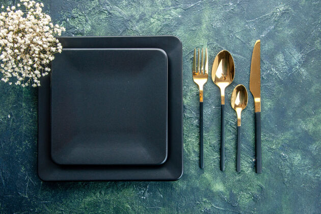 封闭顶视图黑色方形盘子 带金色叉子 勺子和刀 背景为深蓝色晚餐厨房餐厅餐具颜色背景晚餐厨房