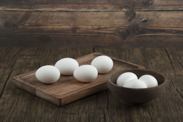 碗木质背景上放满有机生鸡蛋的木板和碗鸡肉易碎家禽