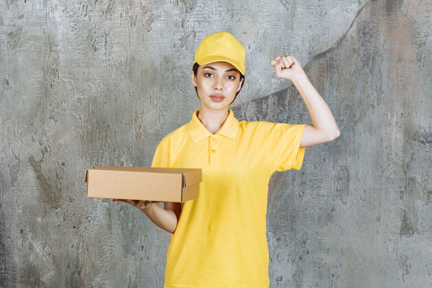 食物身穿黄色制服的女服务人员手持一个纸板箱 并显示积极的手势员工人送货