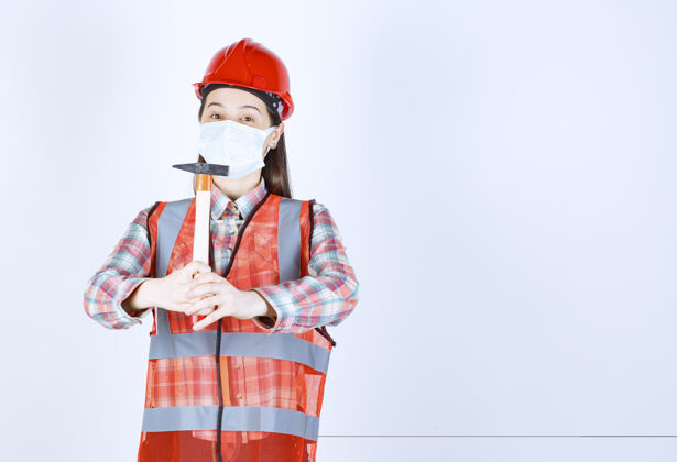 人戴着安全面具 头戴红色头盔 手持木柄斧头的女建筑工程师建筑物制服面罩