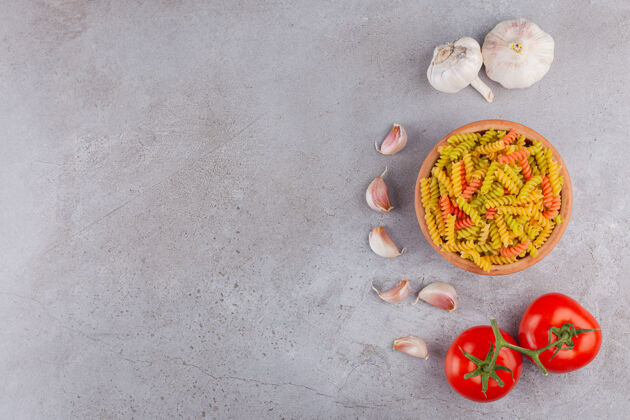 桌子一碗五颜六色的生螺旋意大利面 配大蒜和新鲜的红色西红柿自然面食视图