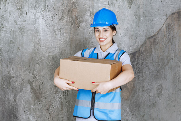 服务身穿蓝色制服 头戴头盔 手持硬纸板包裹的女工程师送货员货物姿势