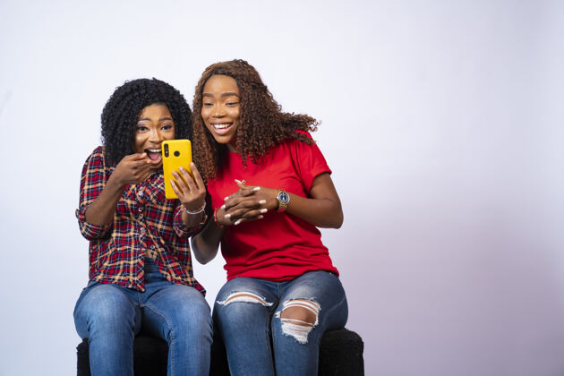 女孩特写两个美丽的黑人妇女看着兴奋 而在一个电话上看内容一起内容尼日利亚女性