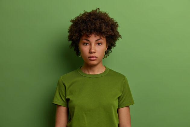 成人认真果断的千禧一代美国黑人女性直视 看起来自信 穿着休闲绿色t恤 在室内摆姿势 听信息 直奔事业严肃表达休闲