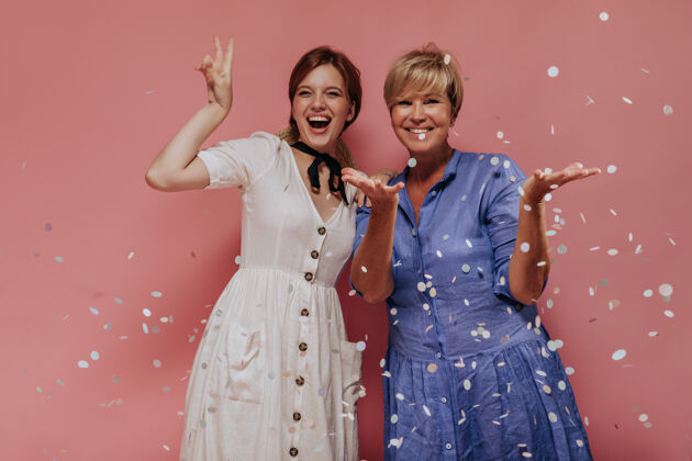 短发情绪化的两位女士 一头时尚短发 穿着夏日摩登的衣服 笑着 展示着和平的标志 在粉色的背景下摆出五彩纸屑的姿势女儿中等室内