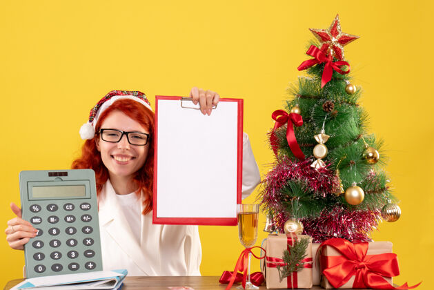 颜色前视图女医生拿着计算器围着圣诞礼物和圣诞树庆祝圣诞丝带