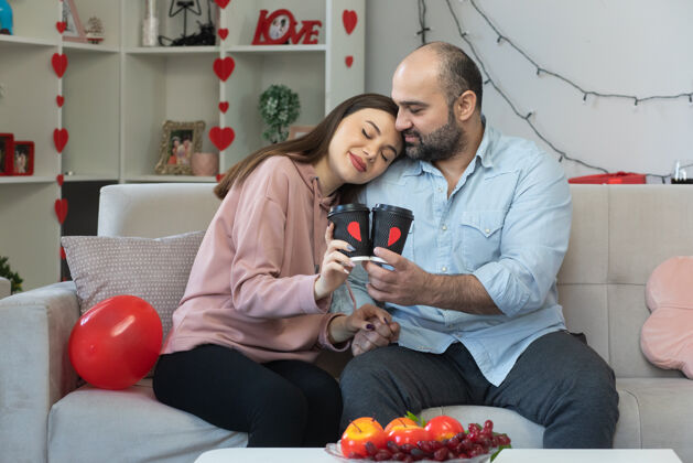 庆祝年轻漂亮的夫妇幸福的男女拿着咖啡杯幸福的恋爱在一起拥抱庆祝国际妇女节坐在客厅的沙发上女人房间在一起