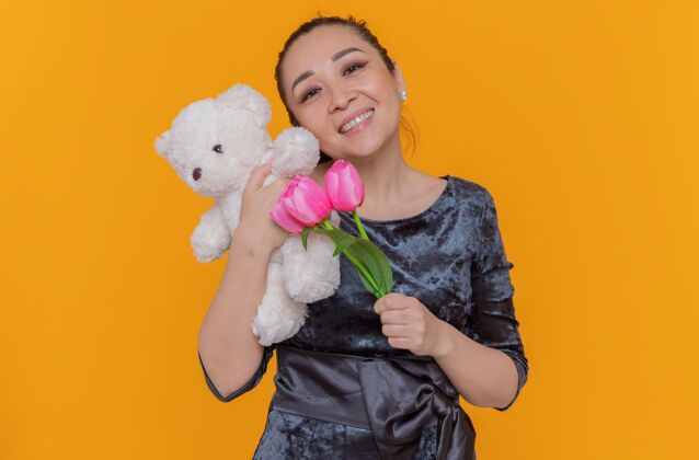 郁金香快乐而积极的亚洲女人手持一束粉色郁金香和泰迪熊 站在橘色的墙上欢笑着庆祝国际妇女节快乐欢呼亚洲