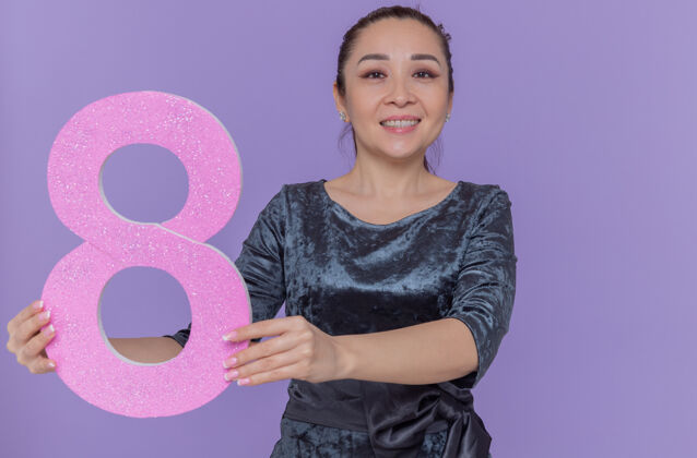 亚洲快乐的亚洲女人拿着纸板做的8号 站在紫色的墙上 面带微笑 兴高采烈地庆祝国际妇女节女人微笑举行