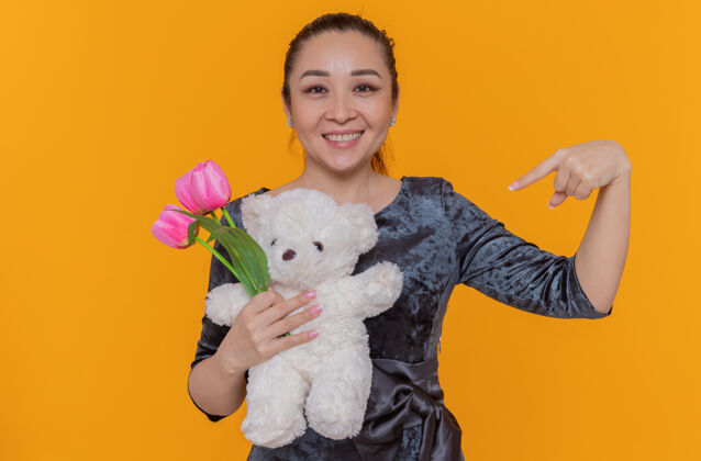 站快乐的亚洲女人捧着粉色郁金香和泰迪熊的花束泰迪国际指向