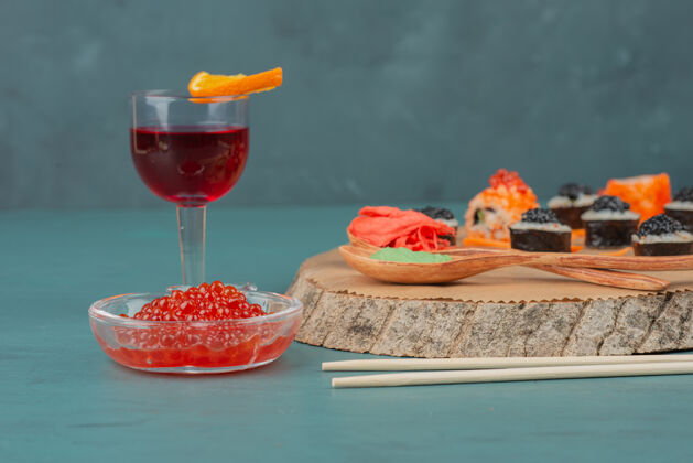 鱼子酱把寿司 红鱼子酱和一杯红酒放在蓝色的桌子上酒麦琪食物