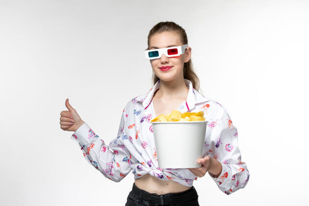 抱着正面图：年轻的女性手提篮里放着薯片 戴着d型太阳镜 浅白色的表面年轻女性电影电影院