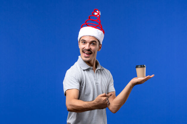 人正面图：年轻男性手持塑料咖啡杯在蓝色墙壁上度假男性新年运动杯子球拍