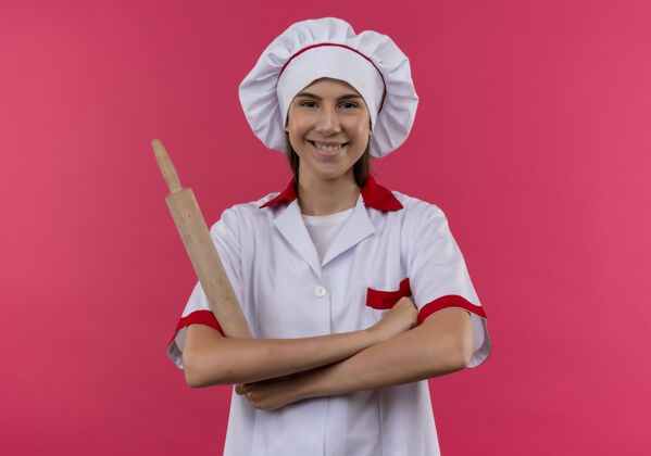 滚动身着厨师制服 面带微笑的白人厨师女孩手拿擀面杖 双臂交叉 在粉色空间与复印空间隔离开来空间粉红微笑