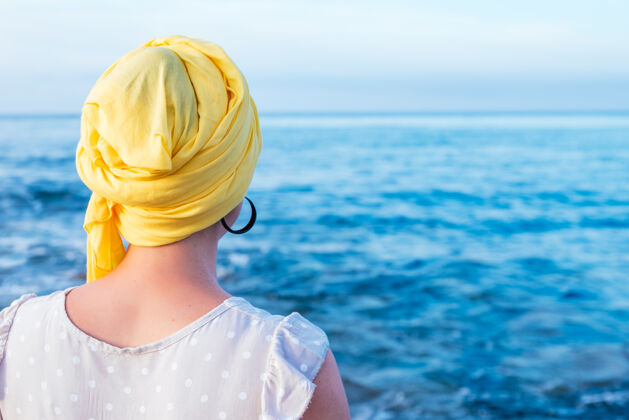 癌症从后面来的一个女人 头上戴着一条黄色的围巾 头上没有头发 正凝视着海的地平线战斗海岸海边