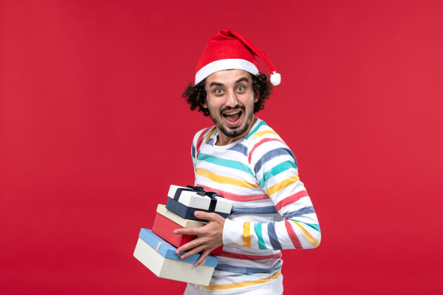 人正面图年轻男性手持节日礼物在红墙假日新年感慨圣诞节人举行