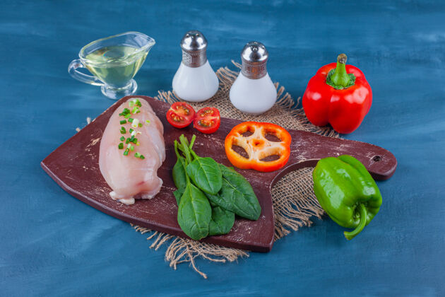 砧板鸡胸肉和蔬菜放在切菜板上 不要用粗麻布餐巾 放在蓝色的桌子上美味家禽鸟