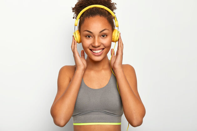 休息年轻女子喜欢音乐作为个人动力 双手戴着耳机 微笑愉快 穿着灰色运动内衣非洲快乐锻炼