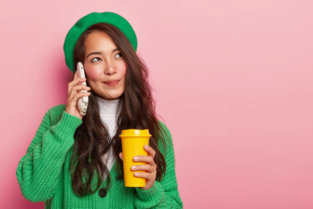 复制空间梦幻可爱的亚洲女孩把智能手机放在耳边 一边喝咖啡一边享受愉快的交谈 留着长长的黑发 穿着绿色时尚的衣服学生饮料电话