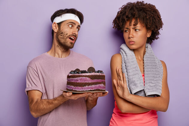 衣服不满的女人做出拒绝的手势 要求不要建议吃甜食 生气地看着拿着美味蛋糕的丈夫站盘子民族