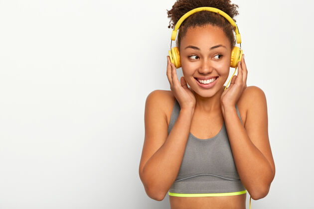运动员快乐的女运动员在运动中感受到乐趣 通过耳机收听音乐播放列表 穿着运动内衣 微笑积极脆运动女人