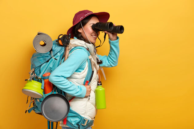 望远镜人 生活方式 度假 旅游理念开朗的女游客用望远镜观察事物 背着背包站着 穿着休闲运动服活动长度成人