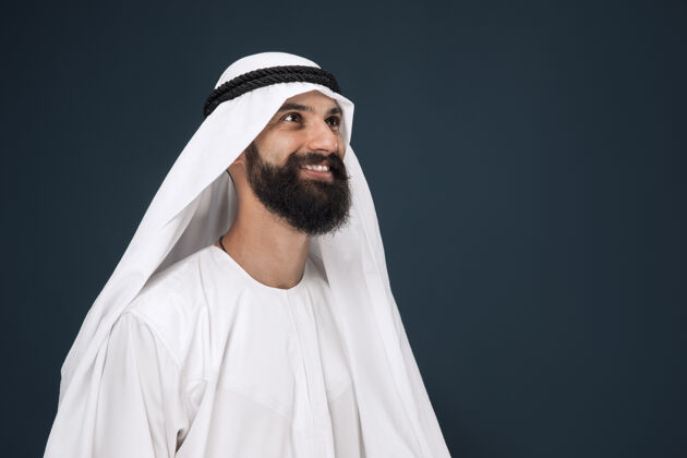 惊人深蓝色墙上的半身阿拉伯沙特商人肖像年轻的男模站着微笑商业概念 金融 面部表情 人类情感东方男人反应