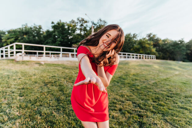 感性迷人的棕色头发的女人在夏天享受户外摄影快乐的笑着穿着红衣服的女模特站在绿色的草地上田野快乐草