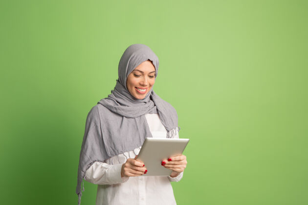 服装戴着头巾的快乐阿拉伯女人拿着笔记本电脑微笑女孩的肖像 在绿色工作室摆姿势情绪成人个人电脑