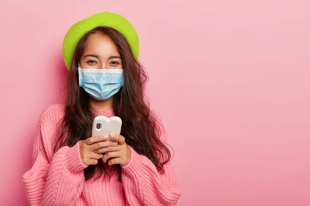 亚洲人心满意足的女人得了流感 戴着防毒面具不传染他人 用手机上网 上网看怎么治病 穿着时髦的衣服流行健康女士