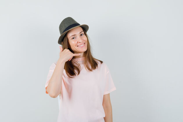 时尚年轻女性穿着粉色t恤 戴着帽子 展示着打电话的姿势 看上去很有帮助 正面视图积极女人电话