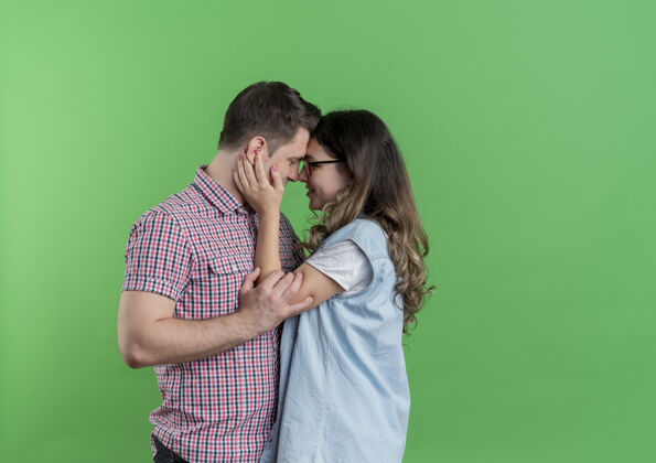 女人一对穿着休闲服的年轻男女站在一起 在绿色的墙上拥抱着幸福的爱情年轻站着衣服