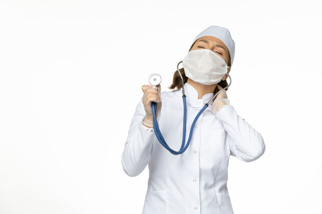 医疗正面图女医生穿着白色医疗服 戴着口罩 在白色办公桌上用听诊器进行大流行性疾病药物病毒隔离女性居家面罩