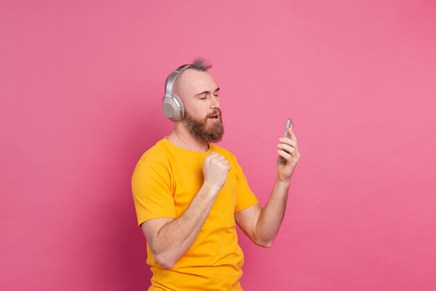 娱乐帅哥带着手机和耳机在粉色背景上翩翩起舞乐趣享受无线