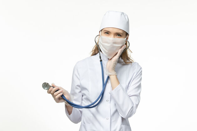 医生正面图：穿着白色医疗服 戴着白色口罩的女医生 在浅白的墙壁上保护自己免受冠状病毒的侵害灯光视野正面