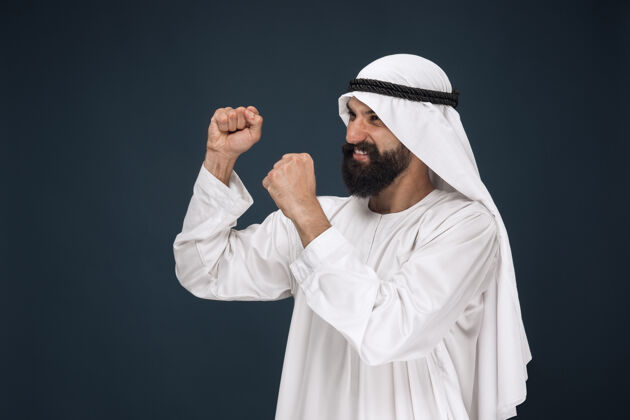 迪拜深蓝色空间上的阿拉伯沙特商人肖像年轻的男模站着 微笑着庆祝男人人类