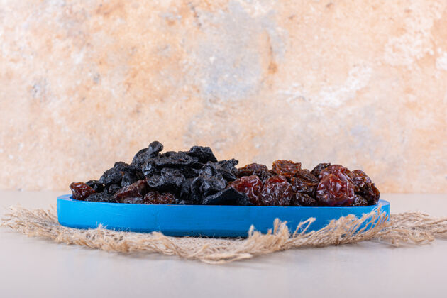 黑蓝色的盘子里装满了干的美味的李子 背景是白色的高质量的照片各种自然甜