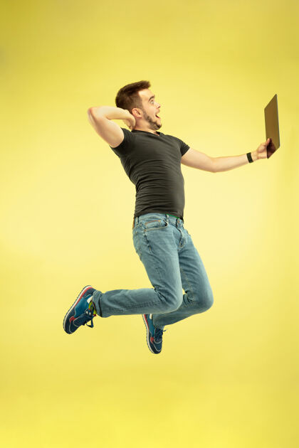 男性失重全长的快乐跳跃的人与黄色背景上孤立的小玩意画像运动办公室技术