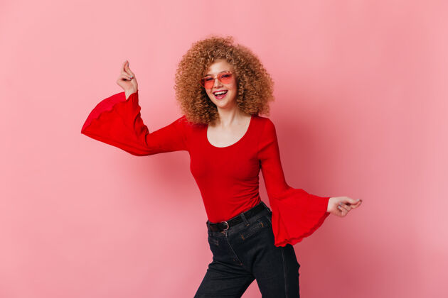 享受一个积极的女孩 穿着红色上衣 宽大的袖子 戴着彩色眼镜 在粉色的空间里翩翩起舞红色衬衫女性优雅