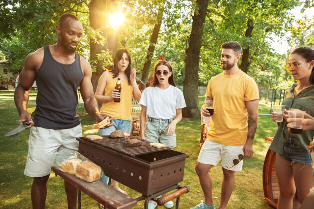 友谊一群快乐的朋友在阳光明媚的日子里喝着啤酒 一起烧烤一起在户外的林间空地或后院休息日落午餐餐