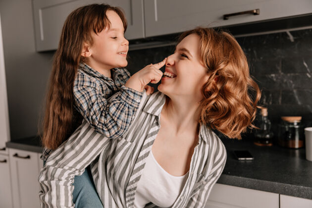 孩子卷发的年轻妈妈和她快乐的小女儿在厨房里的特写镜头女性一起小