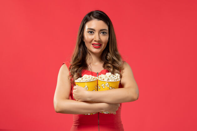 封面女郎正面图年轻女性手持爆米花包 微笑着站在红色的表面上举行包装电影