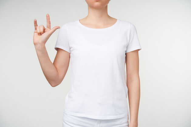 女性摄影棚的照片 年轻女子保持她的手抬起 形成手势 同时使用手语 站在白色背景下的休闲服特写手指手