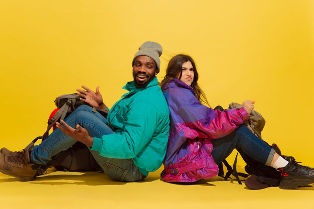 手势不同的情景一对快乐的年轻旅游夫妇的肖像 在黄色的工作室背景上带着孤立的袋子充分年轻人喜悦